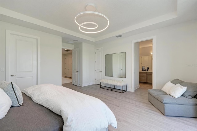 bedroom with ensuite bathroom, visible vents, baseboards, light wood finished floors, and a tray ceiling