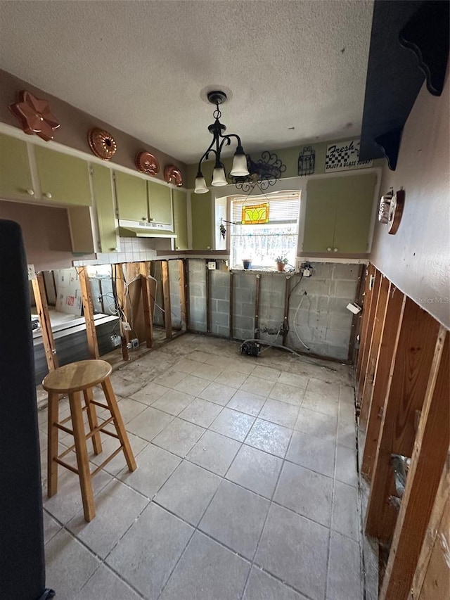 kitchen featuring decorative light fixtures, light tile patterned floors, green cabinets, freestanding refrigerator, and under cabinet range hood