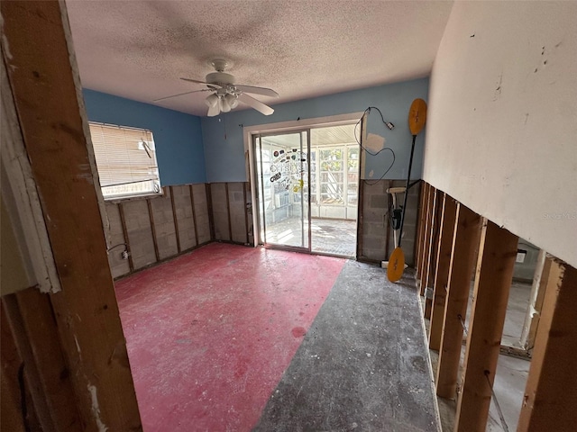 unfurnished living room featuring a wainscoted wall, a textured ceiling, and a ceiling fan