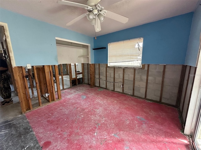 unfurnished bedroom with a ceiling fan and concrete block wall