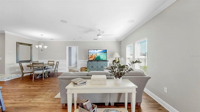 living room with baseboards, ceiling fan with notable chandelier, ornamental molding, and light wood finished floors