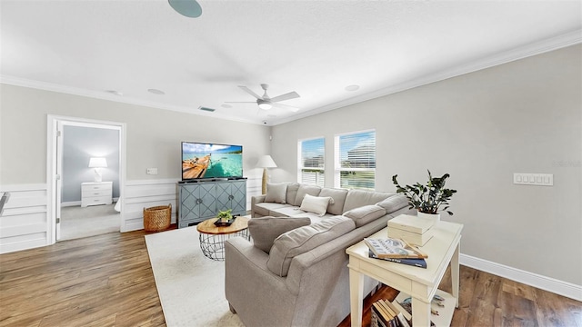 living room featuring visible vents, crown molding, ceiling fan, a wainscoted wall, and wood finished floors