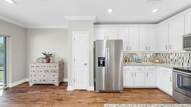 kitchen featuring ornamental molding, stainless steel appliances, white cabinets, light wood-type flooring, and backsplash