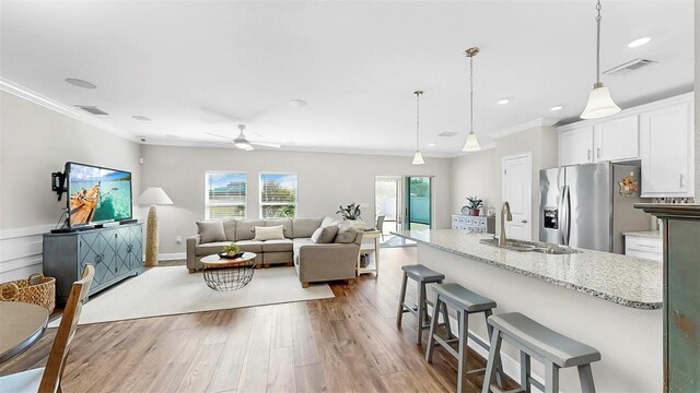 kitchen featuring visible vents, ornamental molding, a sink, stainless steel fridge, and white cabinets