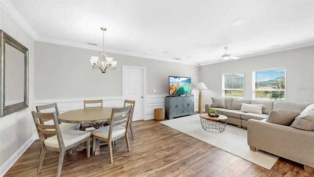 dining space featuring visible vents, ornamental molding, ceiling fan with notable chandelier, wood finished floors, and wainscoting