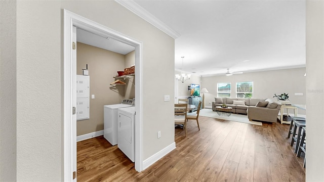 clothes washing area featuring wood finished floors, laundry area, ornamental molding, washer and dryer, and a chandelier