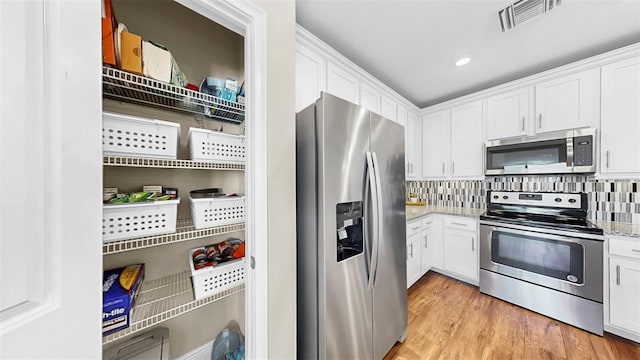 kitchen featuring light stone counters, visible vents, white cabinets, and stainless steel appliances