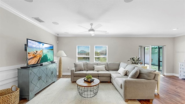 living room featuring a ceiling fan, baseboards, visible vents, light wood finished floors, and ornamental molding