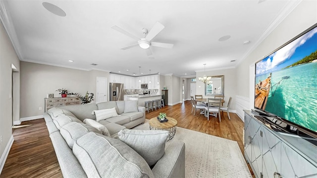 living room featuring ceiling fan with notable chandelier, wood finished floors, baseboards, and ornamental molding