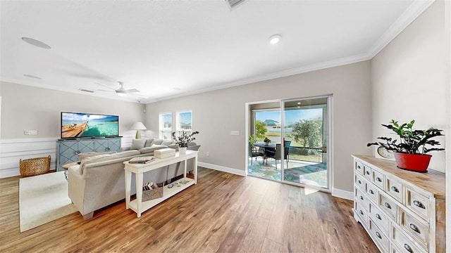 living room featuring a ceiling fan, crown molding, baseboards, and wood finished floors