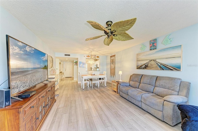 living area featuring a textured ceiling, visible vents, a ceiling fan, baseboards, and light wood finished floors