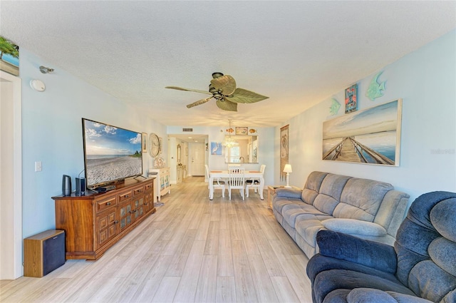living room featuring light wood-style floors, visible vents, a ceiling fan, and a textured ceiling