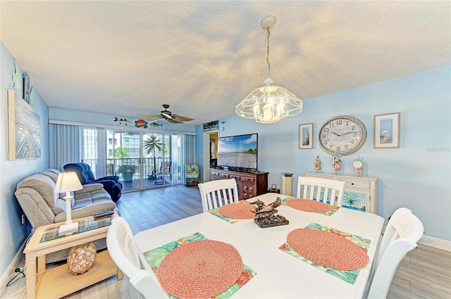 dining room with light wood-style floors, a textured ceiling, baseboards, and ceiling fan with notable chandelier