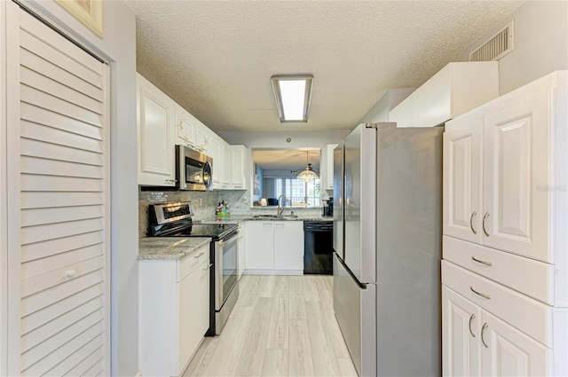 kitchen featuring visible vents, white cabinets, appliances with stainless steel finishes, decorative light fixtures, and a sink