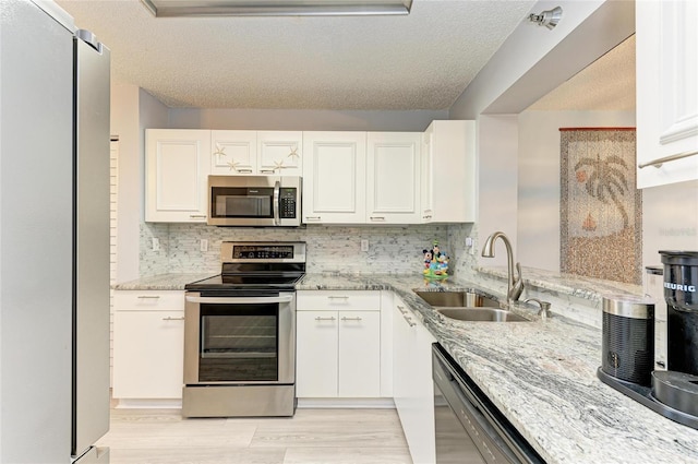 kitchen with appliances with stainless steel finishes, a sink, light stone counters, and white cabinets