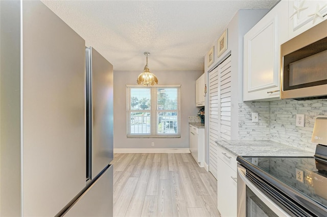 kitchen featuring appliances with stainless steel finishes, pendant lighting, white cabinets, and light stone countertops