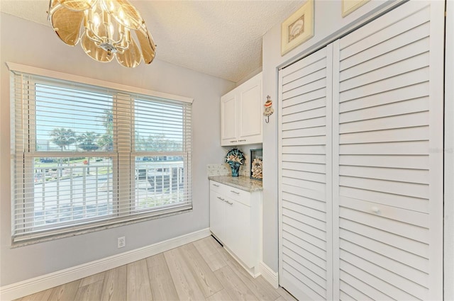 kitchen with light stone counters, light wood finished floors, white cabinets, a textured ceiling, and baseboards