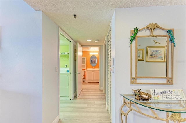 hallway featuring a textured ceiling, washer / clothes dryer, light wood finished floors, and baseboards