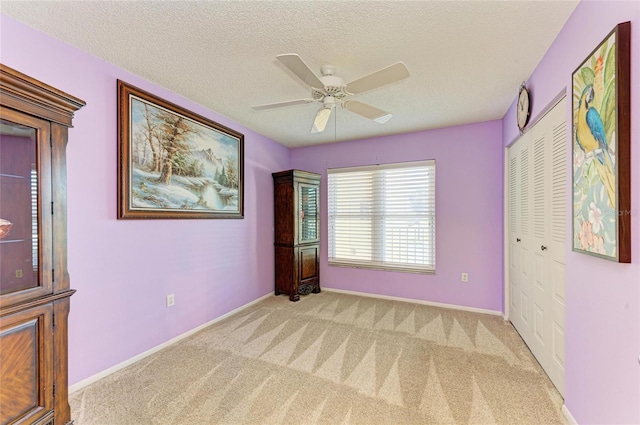 empty room featuring light carpet, a textured ceiling, and baseboards