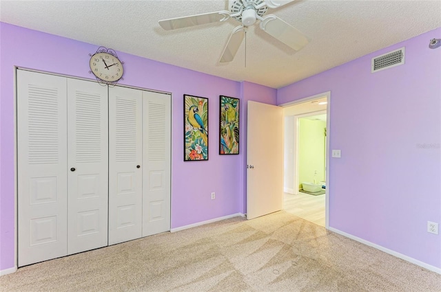 unfurnished bedroom featuring a textured ceiling, ceiling fan, light colored carpet, visible vents, and a closet