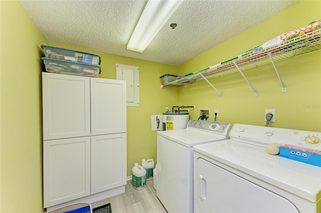 laundry area featuring cabinet space, water heater, light wood-style floors, a textured ceiling, and separate washer and dryer