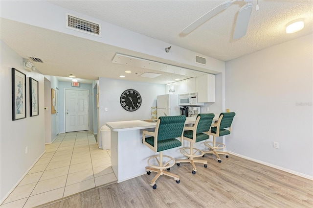 interior space featuring white appliances, a breakfast bar, visible vents, white cabinetry, and light countertops