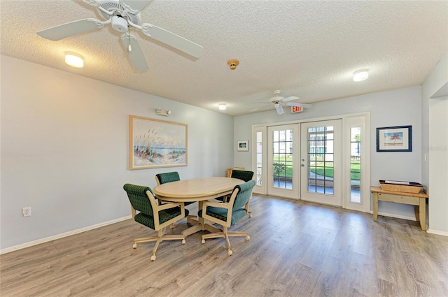 dining space with french doors, light wood-style flooring, baseboards, and a textured ceiling