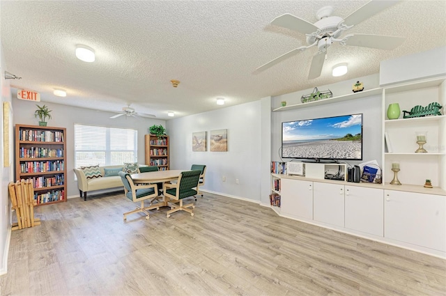 interior space featuring a ceiling fan, baseboards, a textured ceiling, and light wood finished floors