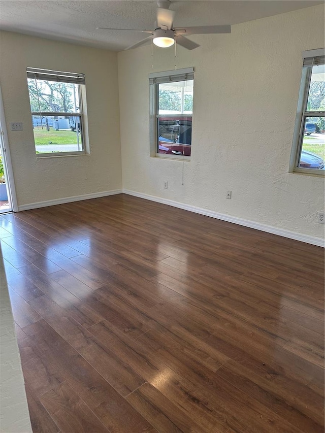 empty room with a healthy amount of sunlight, a textured wall, a textured ceiling, and wood finished floors