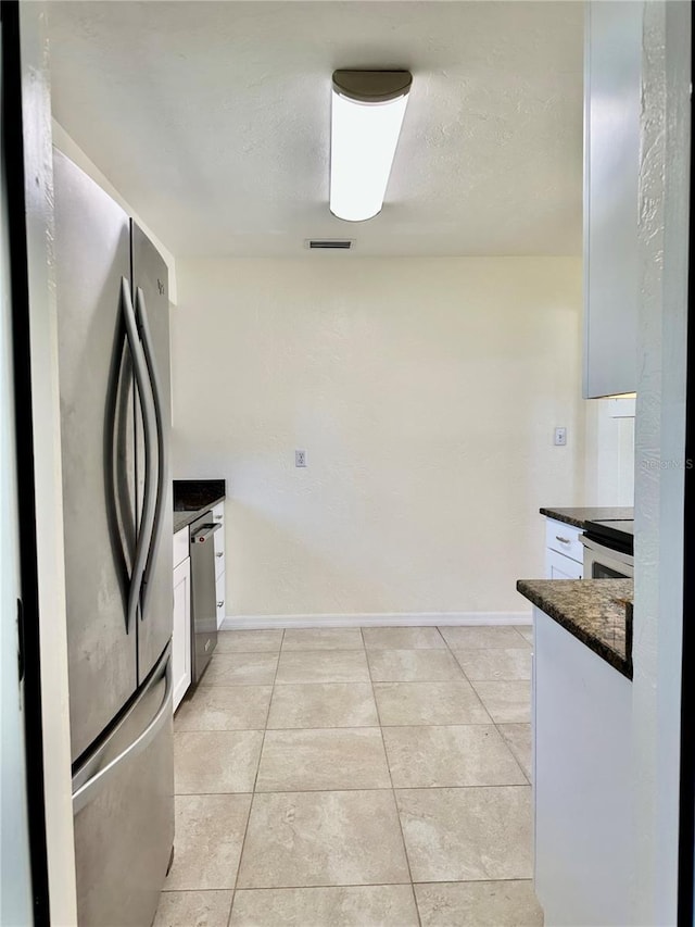 kitchen featuring light tile patterned floors, dark countertops, appliances with stainless steel finishes, white cabinets, and baseboards