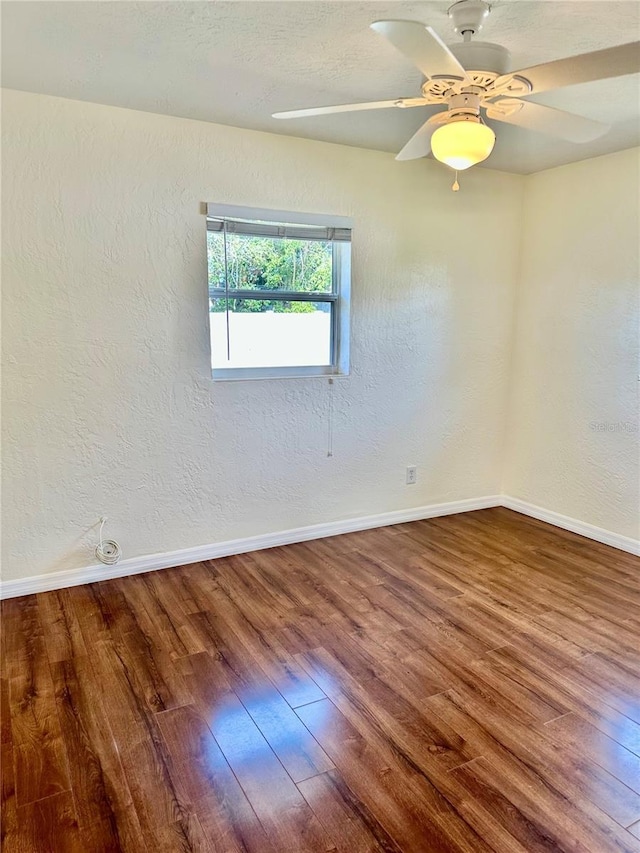 empty room with a textured wall, baseboards, and wood finished floors