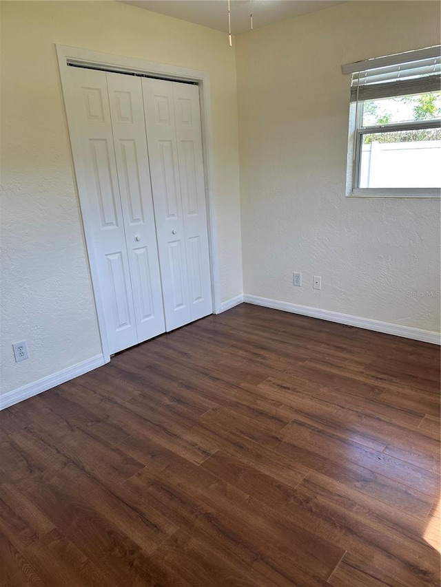 unfurnished bedroom with dark wood-type flooring, a closet, a textured wall, and baseboards