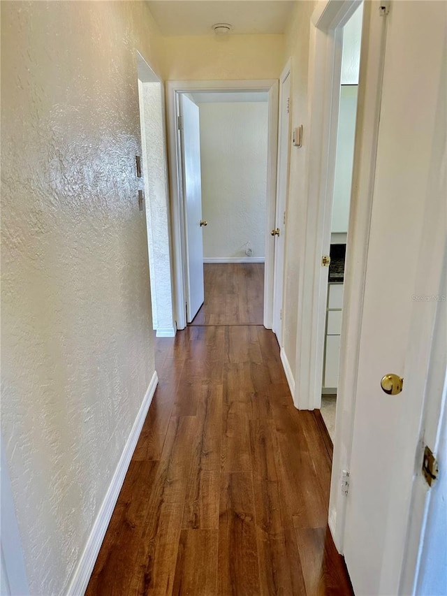 hallway featuring a textured wall, baseboards, and wood finished floors