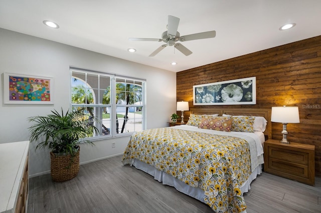 bedroom featuring an accent wall, light wood finished floors, wood walls, and recessed lighting