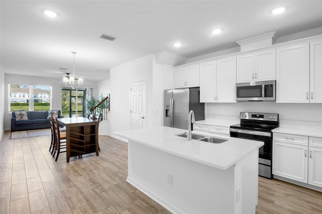 kitchen featuring light wood finished floors, stainless steel appliances, visible vents, a kitchen island with sink, and a sink