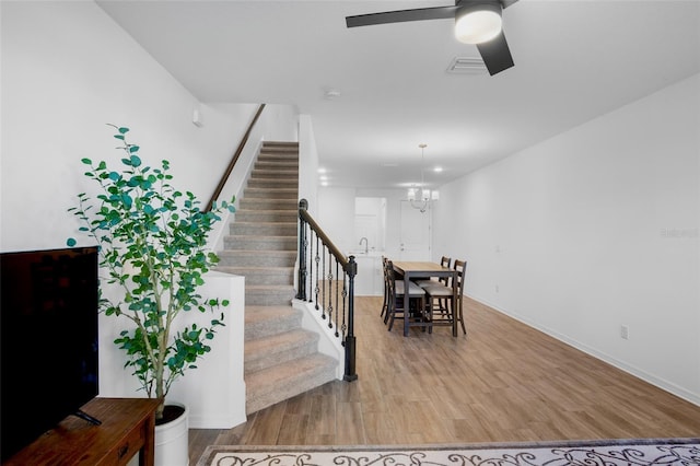 dining space with ceiling fan with notable chandelier, stairway, baseboards, and wood finished floors