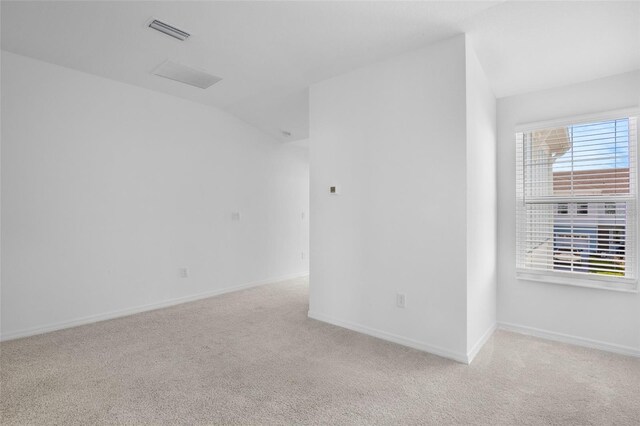 unfurnished room featuring light colored carpet, vaulted ceiling, visible vents, and baseboards