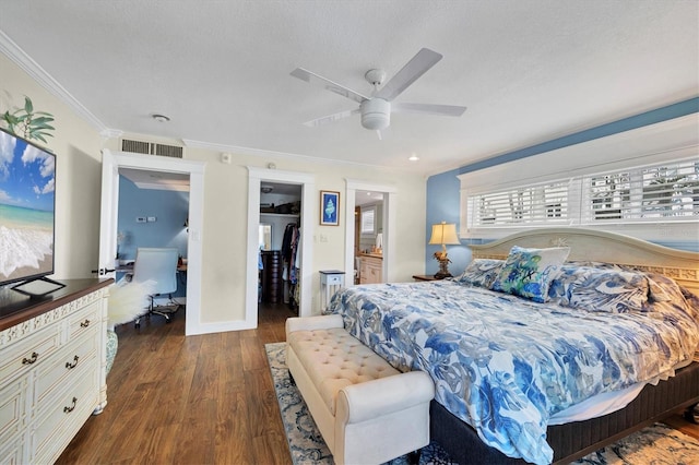 bedroom featuring a textured ceiling, a closet, dark wood-style floors, a walk in closet, and crown molding