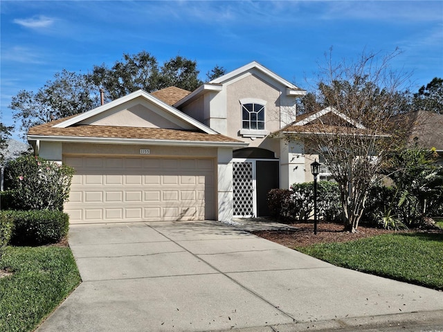 traditional-style house with a garage, roof with shingles, concrete driveway, and stucco siding