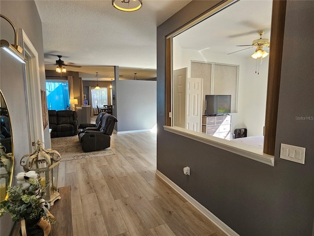 hall with baseboards, light wood-style flooring, and a textured ceiling