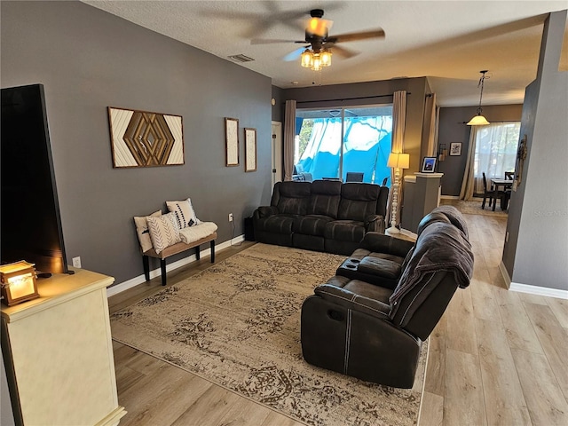 living area featuring a ceiling fan, light wood-style flooring, visible vents, and baseboards