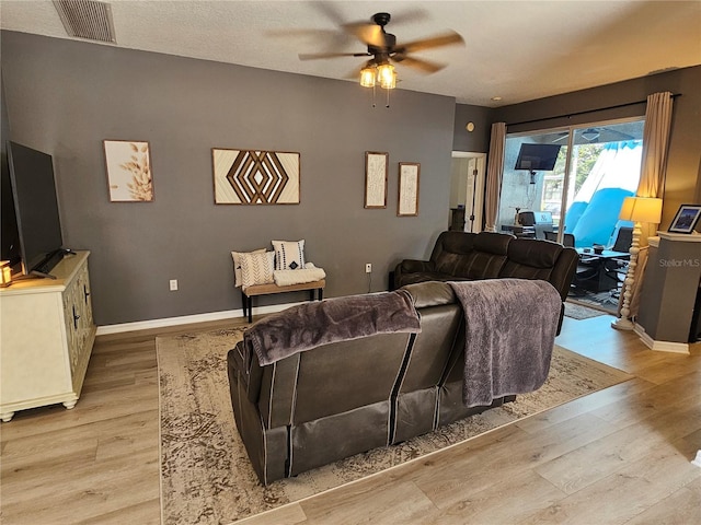 living area featuring baseboards, light wood-style flooring, visible vents, and a ceiling fan