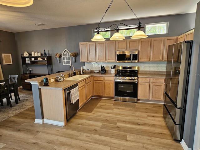 kitchen featuring pendant lighting, stainless steel appliances, light countertops, a sink, and a peninsula