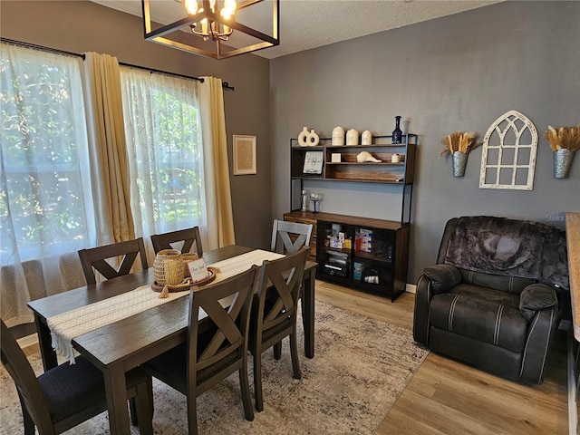 dining room with light wood-type flooring, a notable chandelier, baseboards, and a textured ceiling