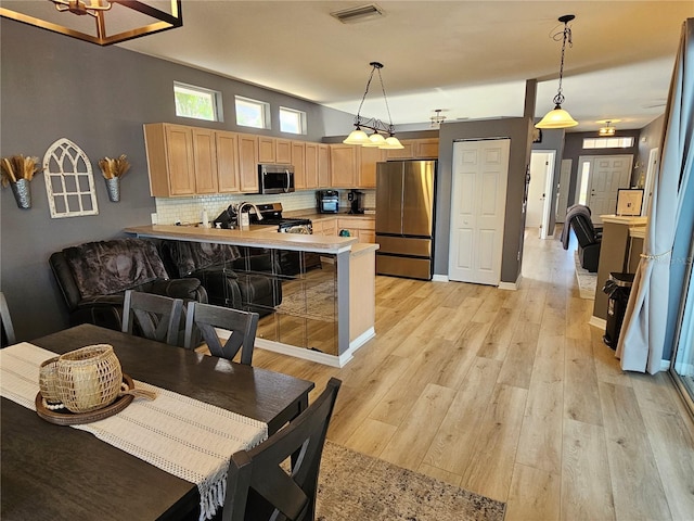 kitchen featuring visible vents, a peninsula, stainless steel appliances, light countertops, and pendant lighting