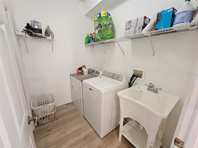 laundry room with laundry area, light wood-style floors, separate washer and dryer, and a sink