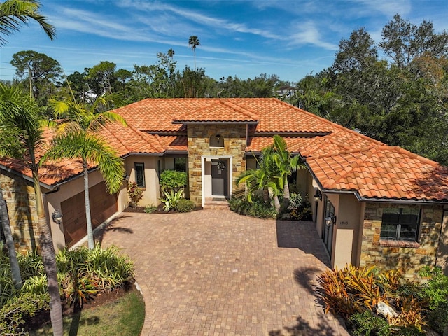 mediterranean / spanish house featuring stone siding, a tile roof, an attached garage, decorative driveway, and stucco siding