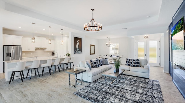 living area featuring light wood-style flooring, recessed lighting, french doors, a raised ceiling, and an inviting chandelier