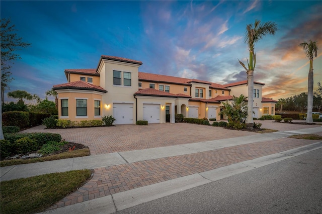 townhome / multi-family property with driveway, a tiled roof, a garage, and stucco siding