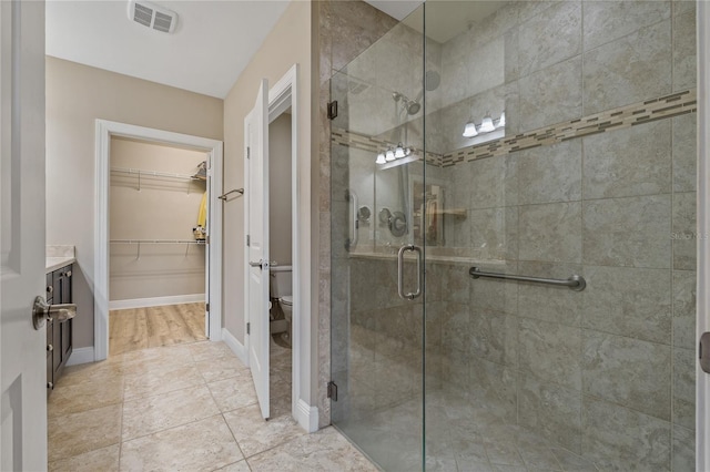 bathroom with toilet, visible vents, baseboards, a shower stall, and a walk in closet